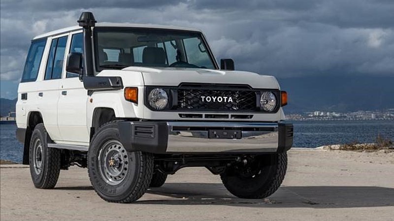 A white Toyota Landcruiser 70 Series SUV with a new look is parked on a sandy area near water.