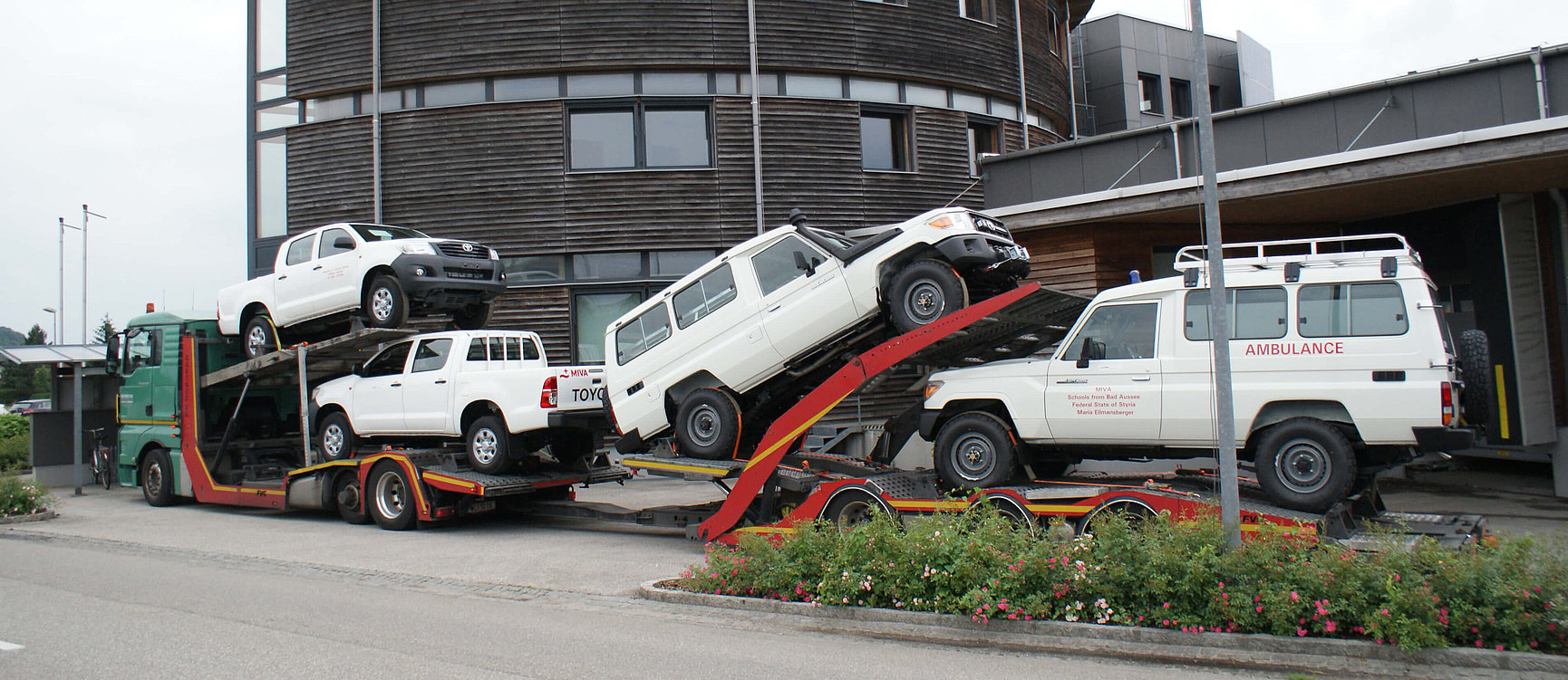 A lorry transports four white Toyota vehicles, including two ambulances, on a multi-storey car transporter.